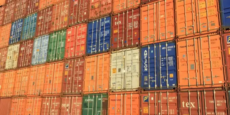 Múltiples contenedores de transporte metálicos de diversos colores apilados en una terminal de carga.
