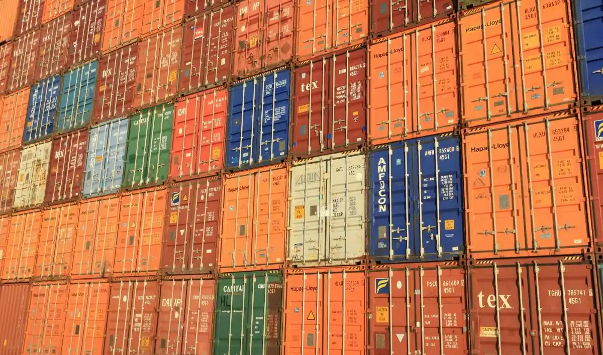 Múltiples contenedores de transporte metálicos de diversos colores apilados en una terminal de carga.