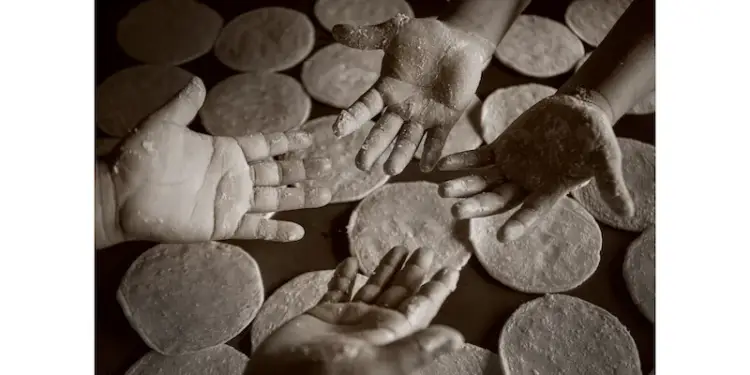 Fotografía en sepia de manos cubiertas de harina sobre discos de masa, simbolizando el trabajo manual y la producción artesanal de alimentos.