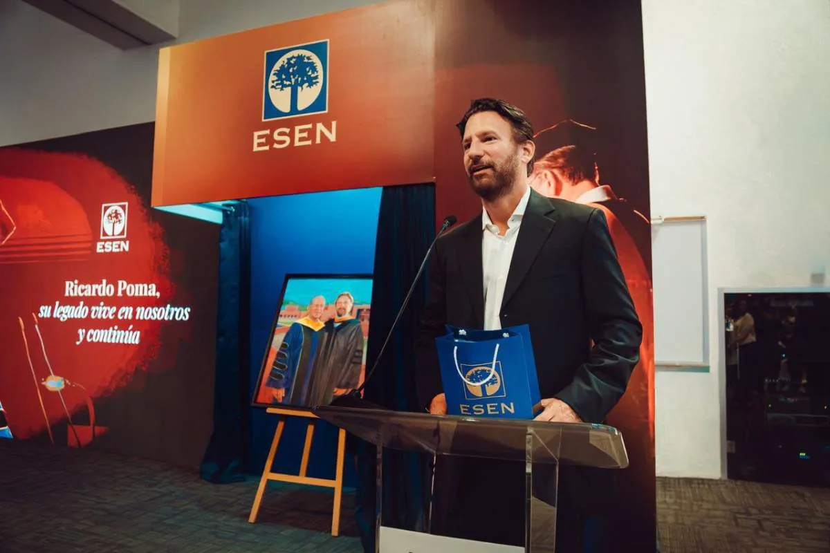 Un hombre con traje oscuro habla en un podio frente a un fondo con el logo de ESEN y una imagen de dos graduados.