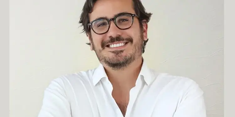 Hombre profesional con gafas y camisa blanca sonriendo ante la cámara con fondo neutro
