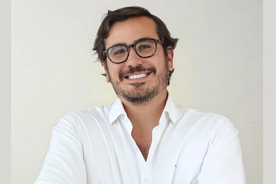Hombre profesional con gafas y camisa blanca sonriendo ante la cámara con fondo neutro