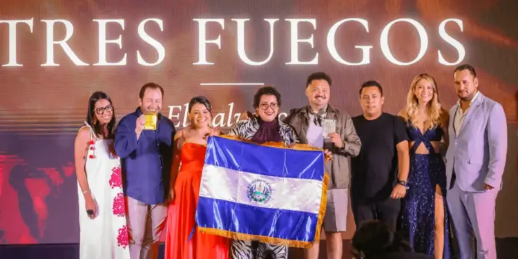 Grupo de ocho personas posando en un escenario frente a un cartel que dice TRES FUEGOS, sosteniendo una bandera y premios.
