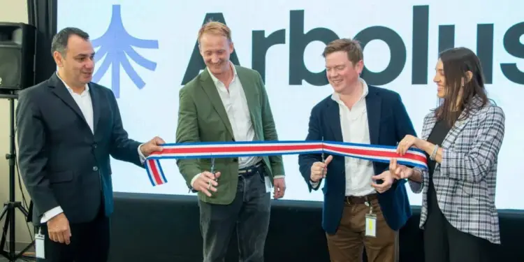 Cuatro profesionales, tres hombres y una mujer, cortan una cinta tricolor con tijeras en una inauguración de negocios. Fondo con logo y texto 'Arbolus'.