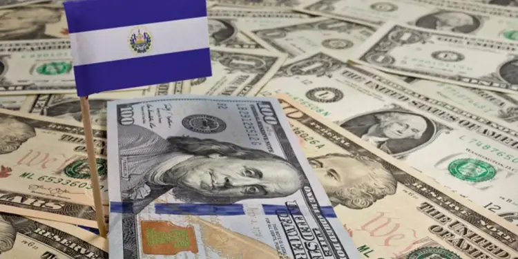 Bandera pequeña de El Salvador colocada sobre un fondo de billetes de dólares estadounidenses en efectivo.
