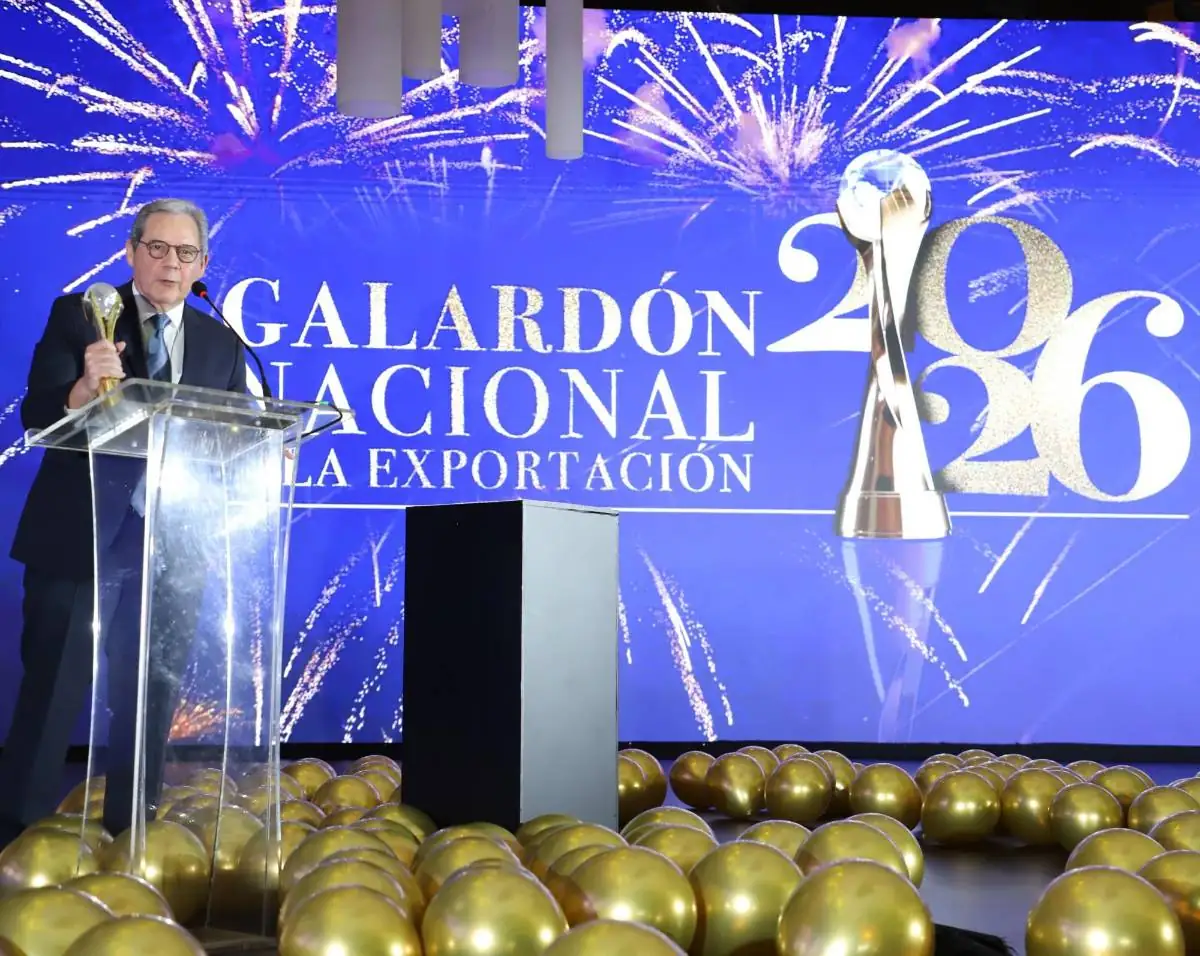 Hombre de traje hablando en un atril frente a una pantalla azul que dice Galardón Nacional de la Exportación