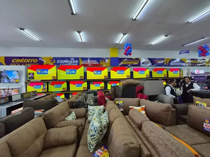 Vista interior de una tienda de electrodomésticos y muebles con sofás en primer plano y televisores en exhibición al fondo.