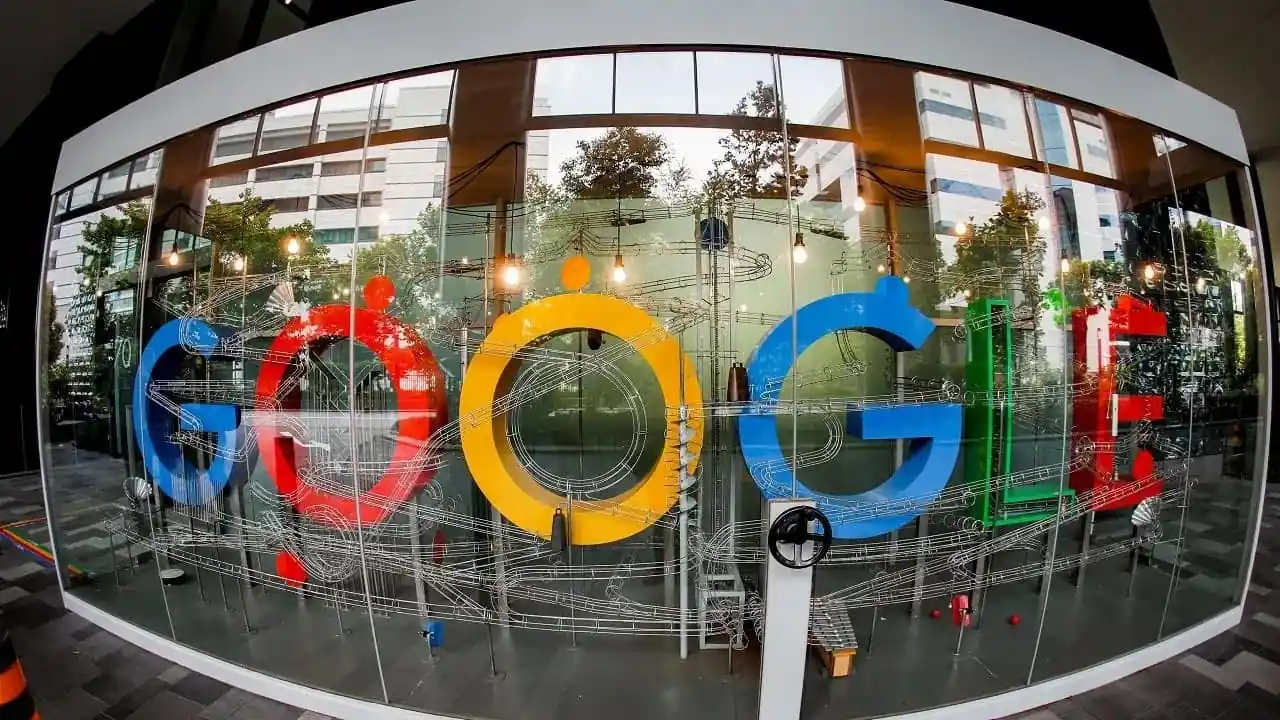 Gran letrero de Google rodeado por un intrincado circuito de canicas dentro de una estructura de cristal en una oficina.