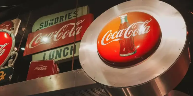 Colección de letreros y anuncios vintage iluminados de Coca-Cola colgando en un establecimiento comercial.