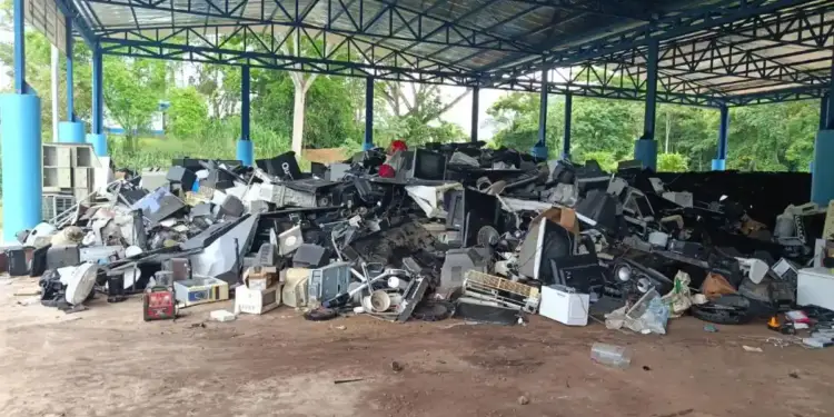 Gran pila de residuos electrónicos (e-waste) bajo un techo metálico azul, mostrando monitores, televisores y componentes de computadora desechados. Representa el desafío del reciclaje.