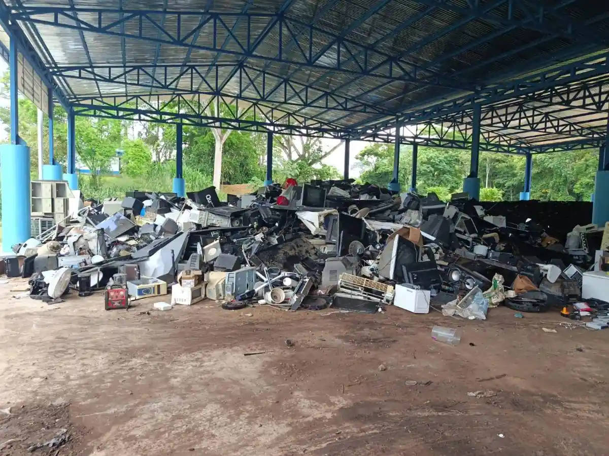 Gran pila de residuos electrónicos (e-waste) bajo un techo metálico azul, mostrando monitores, televisores y componentes de computadora desechados. Representa el desafío del reciclaje.