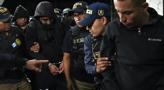Agentes de policía uniformados escoltan a varios hombres esposados durante un operativo nocturno.