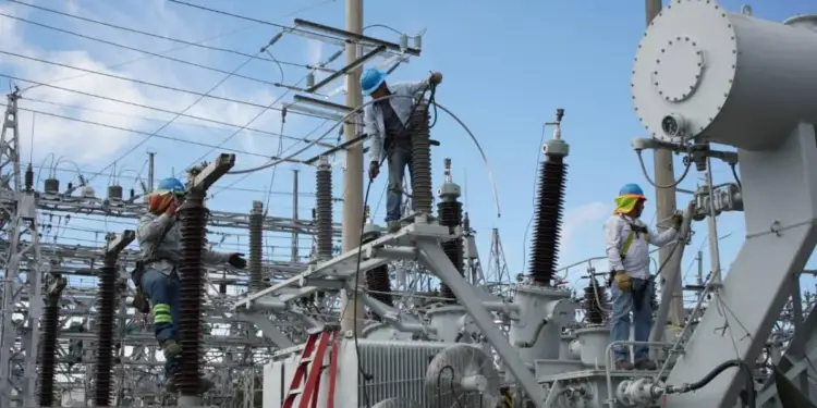 Tres operarios con equipo de seguridad trabajando en el mantenimiento de una subestación eléctrica al aire libre.