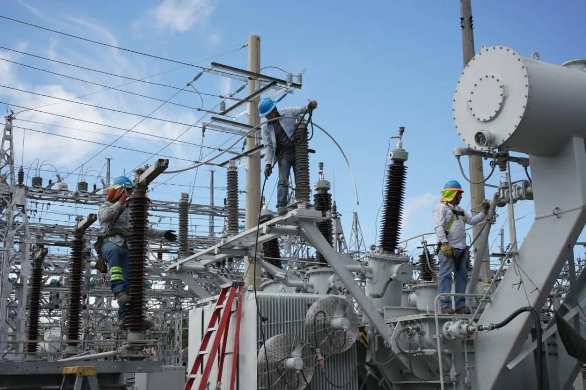 Tres operarios con equipo de seguridad trabajando en el mantenimiento de una subestación eléctrica al aire libre.