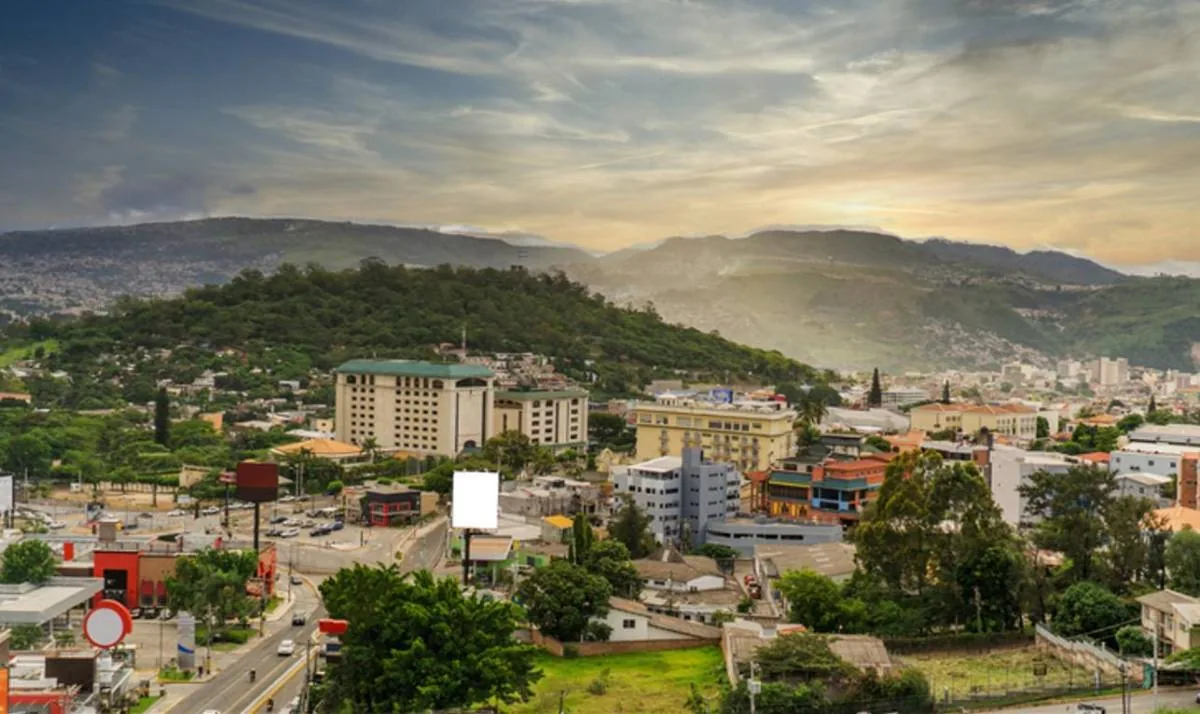 Vista aérea de una ciudad en un valle, con edificios comerciales, residenciales y carreteras. Montañas verdes rodean el área urbana bajo un cielo nublado.
