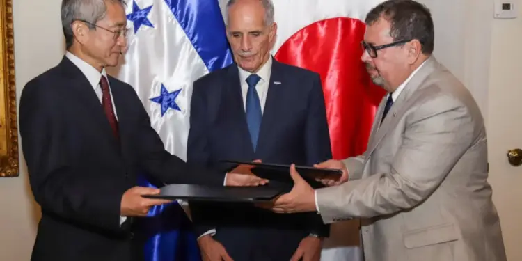 Tres hombres de negocios en trajes formales intercambian documentos frente a las banderas de Honduras y Japón, simbolizando un acuerdo bilateral.