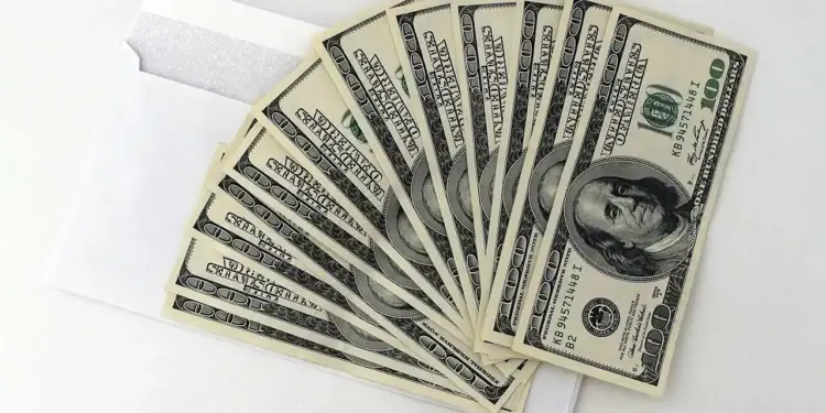 Billetes de cien dólares estadounidenses en abanico sobre un sobre blanco.