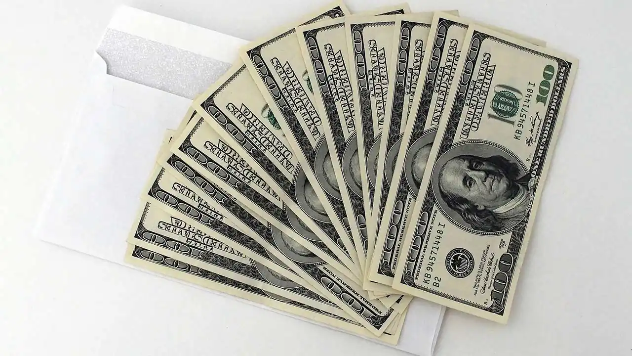 Billetes de cien dólares estadounidenses en abanico sobre un sobre blanco.