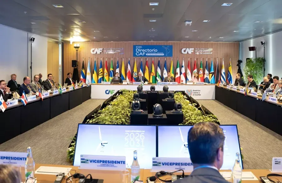 Amplia sala de conferencias con una gran mesa en U, múltiples delegados y banderas internacionales al fondo.