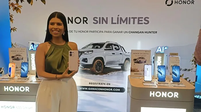Mujer sonriente sosteniendo un teléfono móvil en un stand promocional de la marca HONOR con camioneta de fondo.