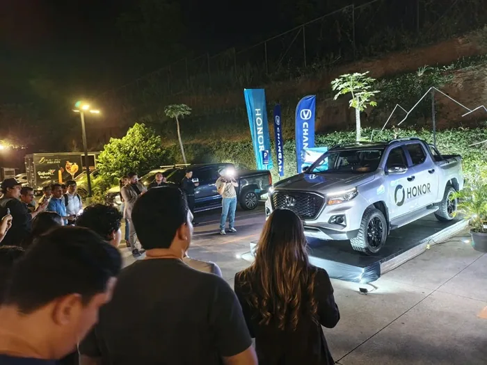 Grupo de personas observando una camioneta pickup gris exhibida en una plataforma durante un evento corporativo nocturno.