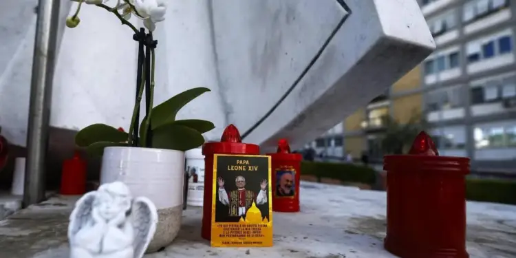 Pequeño monumento con una planta de orquídeas blancas, una pequeña figura de ángel y varias velas rojas encendidas.