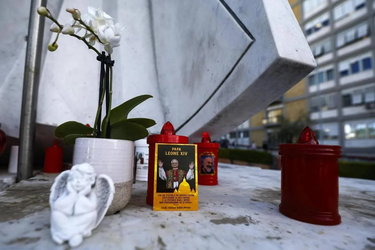 Pequeño monumento con una planta de orquídeas blancas, una pequeña figura de ángel y varias velas rojas encendidas.