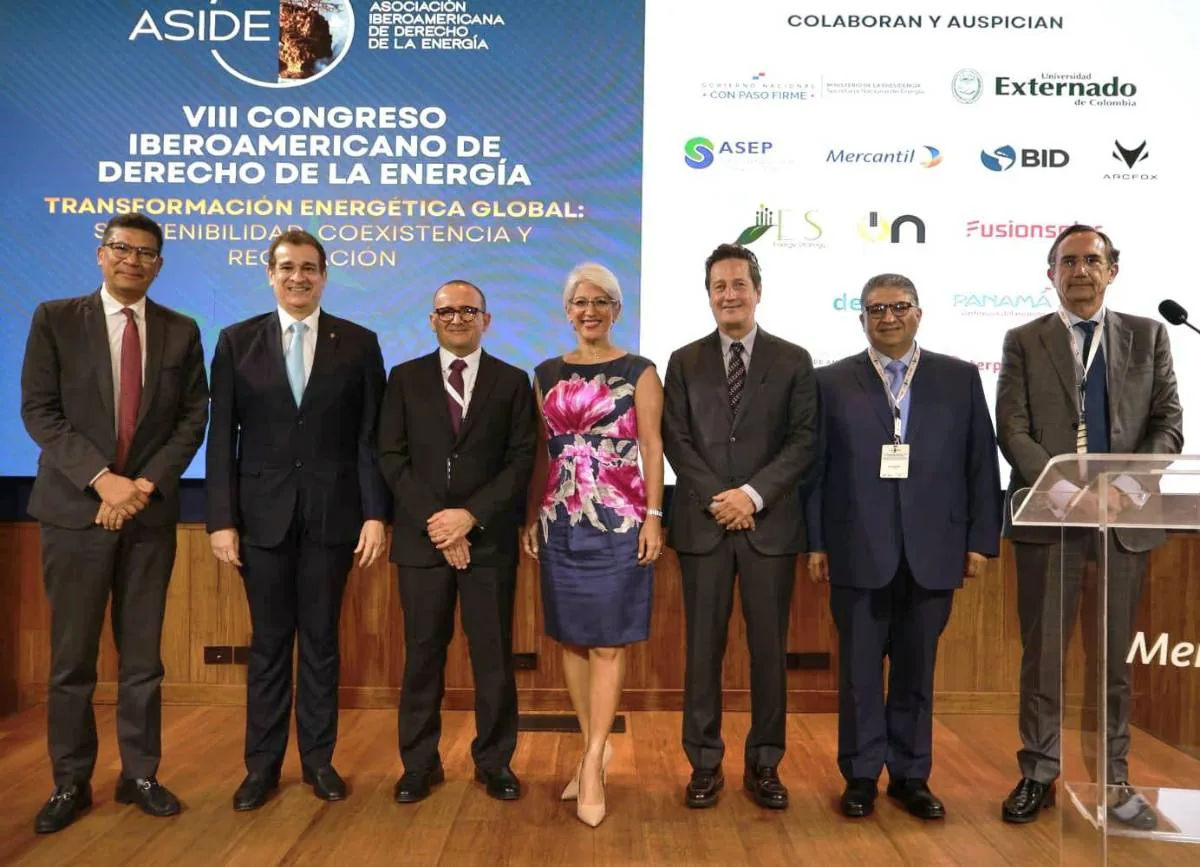 Grupo de profesionales posando para una foto en un evento sobre derecho energético, con un fondo que muestra el título del congreso y logos de patrocinadores.