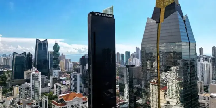 Vista aérea de un distrito financiero con rascacielos modernos, incluyendo el edificio Towerbank y otras estructuras de cristal y oro, bajo un cielo azul. Refleja dinamismo económico.