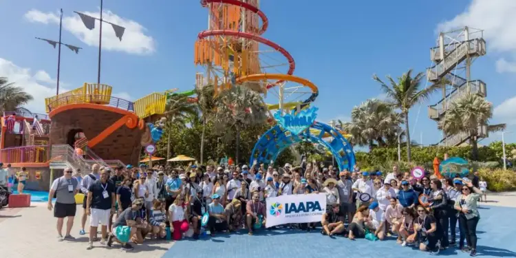 Gran grupo de profesionales de IAAPA América Latina y Caribe posando con un banner frente a atracciones de un parque acuático, incluyendo un barco pirata y toboganes coloridos, bajo un cielo azul.