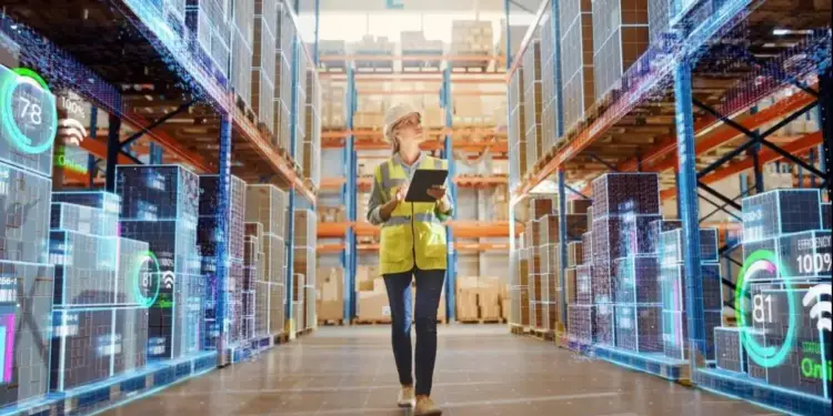 Mujer con casco y chaleco de seguridad camina en almacén moderno con estanterías llenas de cajas y superposiciones digitales de datos de inventario y eficiencia.