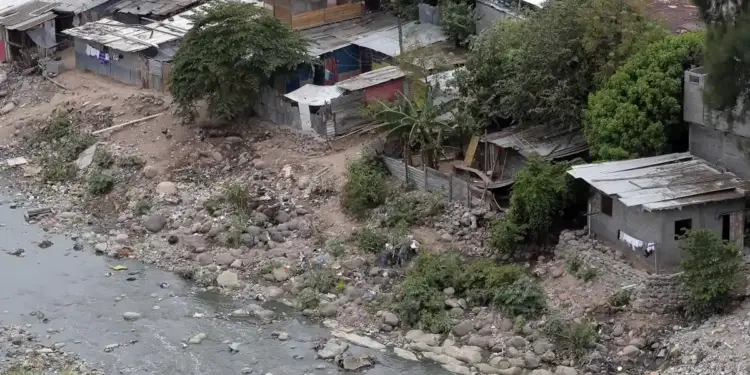 Vista aérea de viviendas precarias y asentamiento informal al lado de un río con rocas y contaminación.