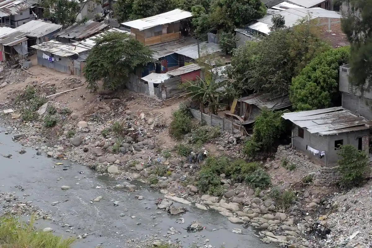 Vista aérea de viviendas precarias y asentamiento informal al lado de un río con rocas y contaminación.