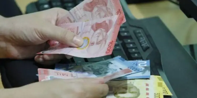 Primer plano de manos sosteniendo billetes de diferentes denominaciones (1000, 2000, 5000) sobre un teclado de computadora, sugiriendo transacciones financieras digitales o contabilidad.