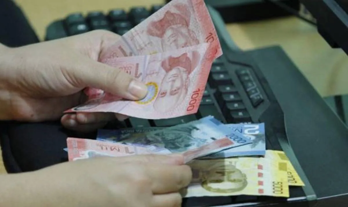 Primer plano de manos sosteniendo billetes de diferentes denominaciones (1000, 2000, 5000) sobre un teclado de computadora, sugiriendo transacciones financieras digitales o contabilidad.
