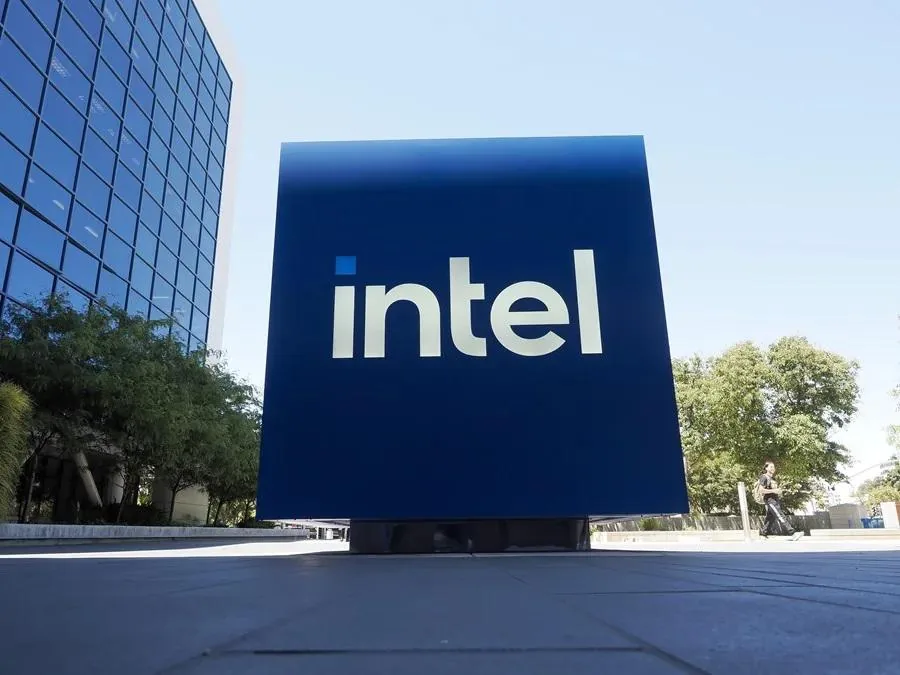 Gran cartel azul con el logotipo de intel frente a un edificio corporativo moderno y árboles en un día soleado.