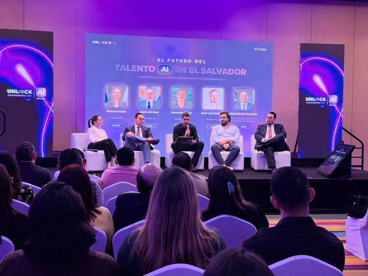 Panel de expertos discutiendo el futuro del talento en IA en El Salvador, con audiencia. Pantalla muestra 'EL FUTURO DEL TALENTO AI EN EL SALVADOR'.