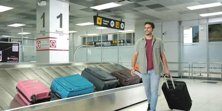 Hombre sonriente con equipaje caminando en la zona de recogida de maletas de un aeropuerto