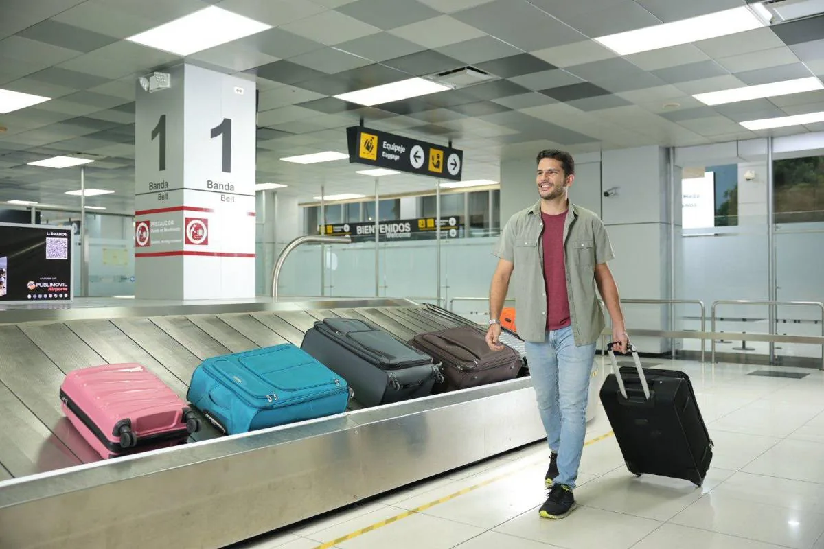 Hombre sonriente con equipaje caminando en la zona de recogida de maletas de un aeropuerto