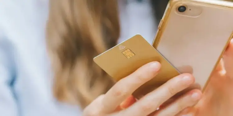 Una persona sostiene un teléfono móvil y una tarjeta bancaria con chip dorado para realizar transacciones financieras.