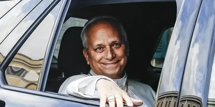 Hombre sonriente con vestimenta clerical asomado por la ventana de un coche oscuro. Reflejos de edificios y cielo en el cristal.