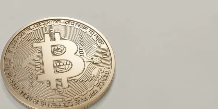 Moneda dorada de bitcoin con el símbolo característico y detalles en relieve sobre un fondo liso gris claro.