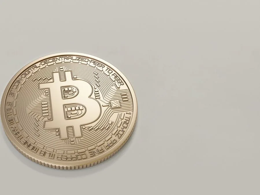 Moneda dorada de bitcoin con el símbolo característico y detalles en relieve sobre un fondo liso gris claro.