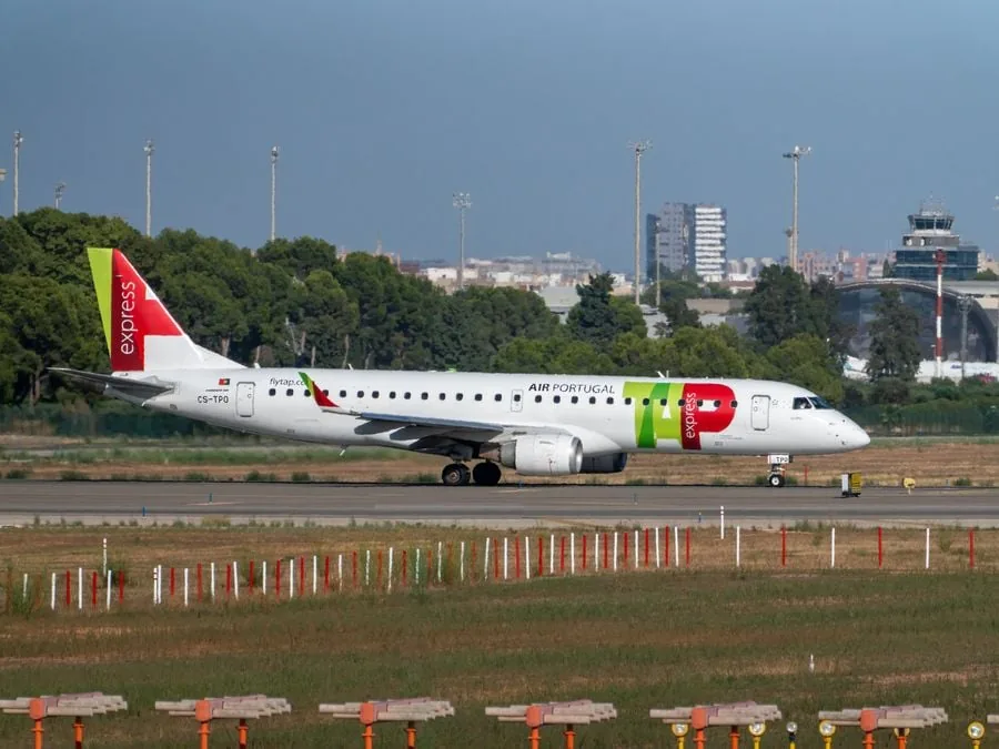 Avión comercial blanco y rojo con la marca AIR PORTUGAL rodando por la pista de un aeropuerto durante el día.