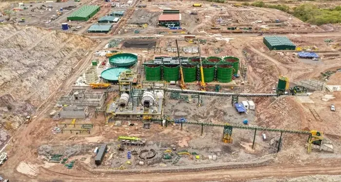 Vista aérea de un gran sitio de construcción industrial con tanques de almacenamiento verdes y maquinaria pesada.