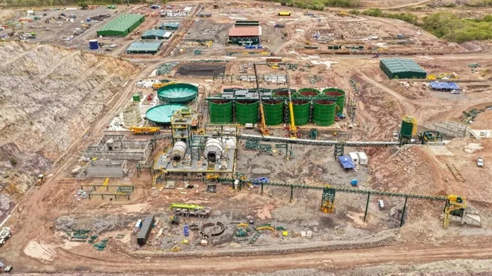 Vista aérea de un gran sitio de construcción industrial con tanques de almacenamiento verdes y maquinaria pesada.