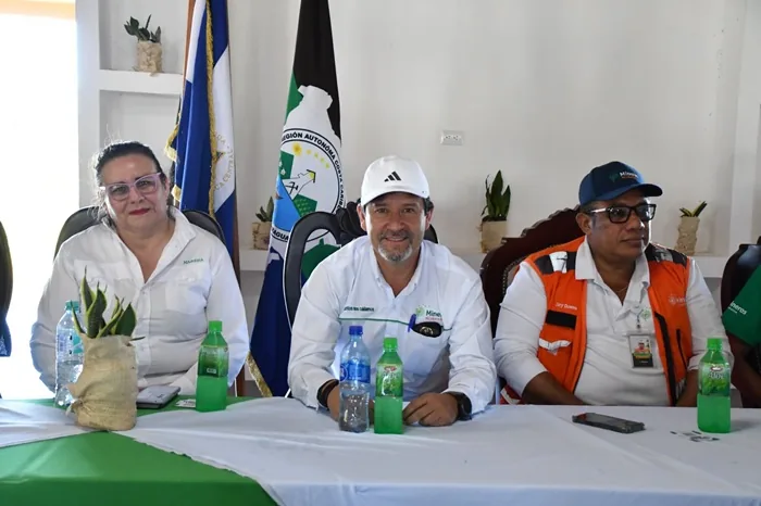 Tres personas sentadas en una mesa de reuniones con banderas al fondo