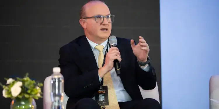 Hombre con traje, corbata y gafas hablando por micrófono en un evento de Business Travel.