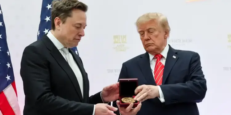 Dos hombres con traje formal sostienen una pequeña caja roja con una medalla dorada frente a banderas de Estados Unidos.
