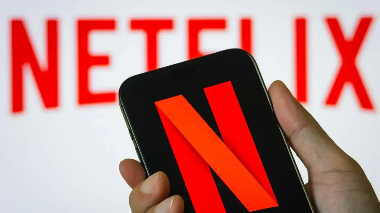 Mano sosteniendo un teléfono inteligente que muestra el logotipo de una empresa de streaming en la pantalla.